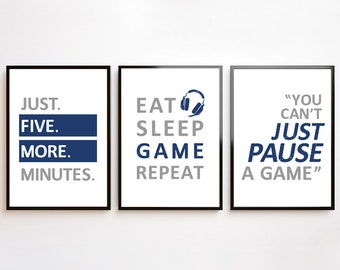 Może przedstawiać: Trzy oprawione wydruki z białymi tłami i czarnymi ramkami. Lewy wydruk głosi "JUST. FIVE. MORE. MINUTES." Środkowy wydruk głosi "EAT SLEEP GAME REPEAT" z niebieską ikoną słuchawek. Prawy wydruk głosi "YOU CAN'T JUST PAUSE A GAME."