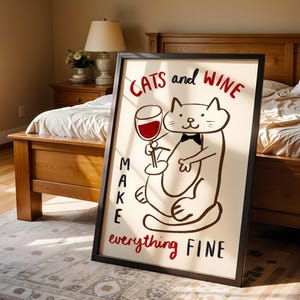 May include: A framed art print with a black border. The print features a cartoon cat holding a wine glass. Text reads "CATS and WINE MAKE everything FINE" in red and black lettering. The artwork is displayed in a bedroom setting.