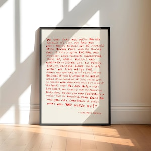 May include: A framed wall art print featuring a cream-colored background with handwritten-style red text. The quote reads: "We don't read and write poetry because it's cute. We read and write poetry because we are members of the human race."