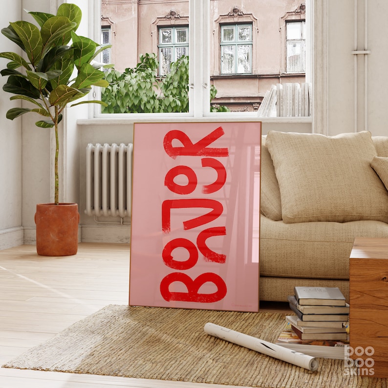 May include: A pink framed poster with the word "BOJOCK" written in red letters. The poster is hanging on a wall in a living room setting.