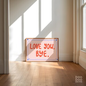 Op de afbeelding: Een roze en witte ingelijste print met blauwe accenten. De print bevat de tekst "Love you, Bye." in rode en blauwe letters.