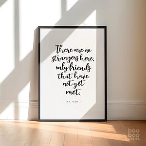 May include: Black and white typography print with the quote "There are no strangers here, only friends that have not yet met." by W.B. Yeats. The print is framed in a black frame and is hanging on a white wall.