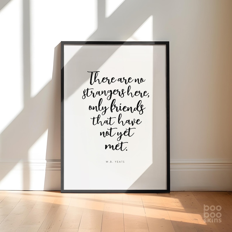 May include: Black and white typography print with the quote "There are no strangers here, only friends that have not yet met." by W.B. Yeats. The print is framed in a black frame and is hanging on a white wall.