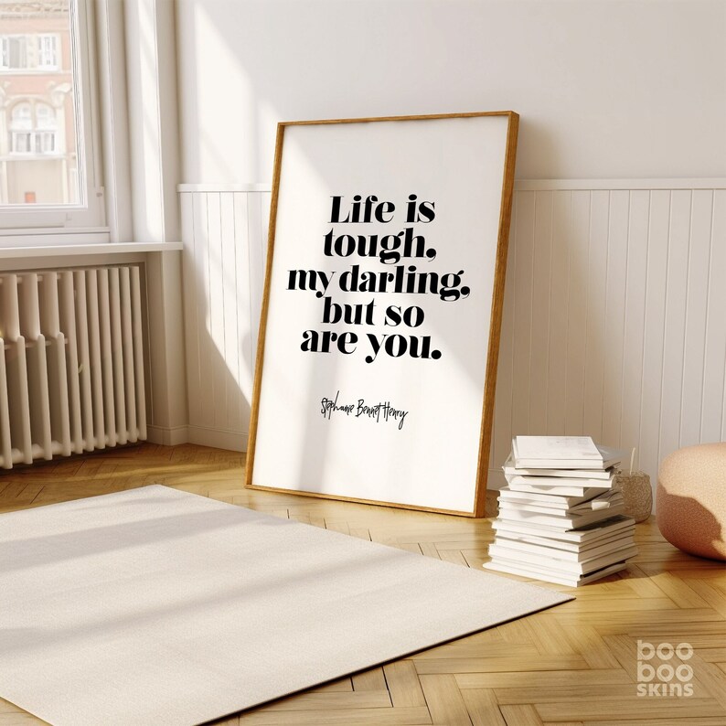 K&ouml;nnte beinhalten: Ein gerahmter Druck mit wei&szlig;em Hintergrund und schwarzem Text, der "Life is tough. my darling. but so are you." lautet. Der Text ist fett gedruckt und zentriert auf der Seite. Die Unterschrift "Stephane Bennett Henry" steht in kleinerer Schrift unter dem Text.