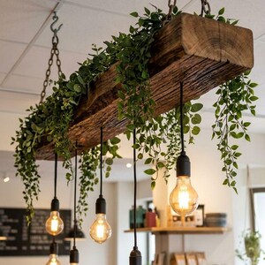 May include: A rustic wooden beam light fixture suspended from chains, adorned with greenery. Six Edison-style light bulbs hang below. The fixture is a decorative element for a cafe or restaurant.
