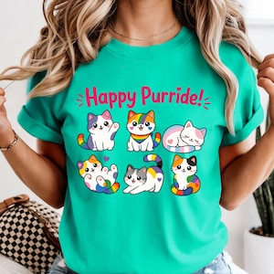 May include: Teal t-shirt featuring the text "Happy Purride!" and cartoon cats with rainbow details. The cats are depicted in different poses, such as waving, sitting, and curled up. The shirt has short sleeves.