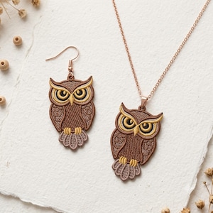 May include: A jewellery set with an owl design, comprising a pendant necklace and earrings. The owl pendants and earrings are brown with yellow and light brown details. The necklace chain and earring hooks are rose gold in colour.
