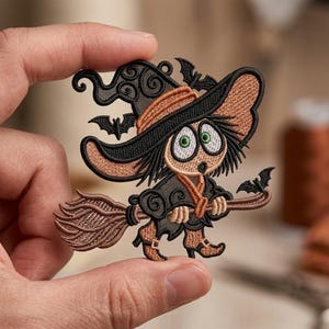 Könnte beinhalten: Ein gestickter Aufnäher mit einer Cartoon-Figur, die einen großen orange-schwarzen spitzen Hut trägt und auf einem braunen Besen reitet. Die Figur hat große weiße Augen mit grünen Iris, schwarzes Haar und drei kleine schwarze Fledermäuse.