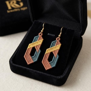 May include: A pair of geometric drop earrings featuring intricate embroidery in shades of mustard yellow, teal, and terracotta. The earrings are suspended from gold-toned metal hooks and are presented inside a black velvet jewelry box.