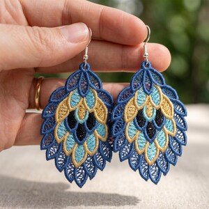 May include: A pair of blue, gold, and black embroidered earrings. The earrings have a teardrop shape with a detailed, openwork design. The earrings are held up by silver-colored hooks.