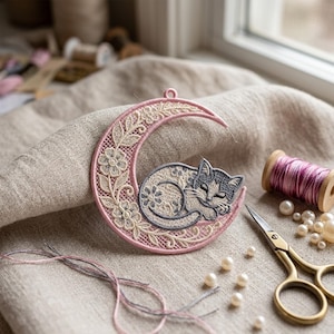 Peut inclure: Broderie en forme de croissant de lune avec un chat endormi. La lune est rose avec des détails de dentelle florale et un chat gris. La broderie est posée sur un fond en lin neutre, avec des fournitures de couture et des perles à proximité.