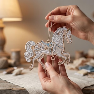 May include: A detailed carousel horse ornament. The horse is cream-coloured with delicate embroidery, accented by light blue and gold details. It has a flowing mane and tail, and a saddle with floral patterns. A beige string is attached for hanging.