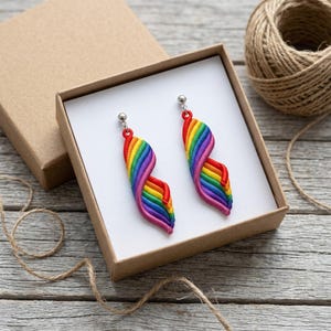 May include: A pair of dangle earrings featuring a twisted, spiral design with vibrant rainbow-colored stripes in red, orange, yellow, green, blue, and purple. Each earring is attached to a small silver-toned metal stud post and sits inside a box.