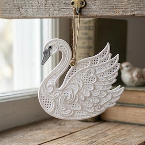 Peut inclure: Ornement en forme de cygne blanc ajouré, avec un bec et un œil gris, suspendu à une poutre en bois. Le cygne présente des motifs détaillés sur les ailes et le corps. Une boucle en ficelle naturelle est utilisée pour la suspension.