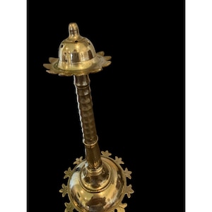 May include: A brass incense burner with a flower-shaped top and base. The stem is textured with a spiral design. The burner is a golden color and stands against a black background.