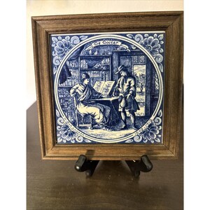 May include: A square ceramic tile in a brown wooden frame featuring a blue and white illustration of a doctor at a desk with a patient. The text reads De Docter, Jan Luyken, and 1649-1712. The scene depicts a room with shelves and a doorway.