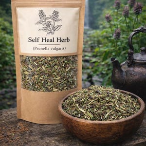 Può includere: Un sacchetto di carta marrone contenente erba essiccata Self Heal (Prunella vulgaris) con un'illustrazione botanica sull'etichetta, accompagnato da una ciotola di legno riempita con la stessa erba essiccata e una teiera in metallo scuro.