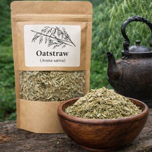May include: A brown paper pouch containing dried oatstraw with a label reading Oatstraw (Avena sativa) and a line drawing of an oat stalk. A wooden bowl filled with the same dried green plant material sits in front of the pouch.