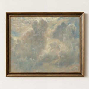 May include: A framed painting of a cloudy sky. The artwork features a palette of soft blues, whites, and beige tones, creating a serene and atmospheric landscape. The frame is a warm, golden brown.