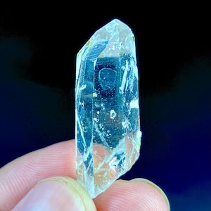 以下が含まれることがあります： 先端が尖った透明で細長い水晶の結晶ポイント。この鉱物標本は、内部の亀裂、自然なインクルージョン、および垂直構造に沿った目に見えるファセットを特徴としており、半透明でガラスのような外観を呈しています。