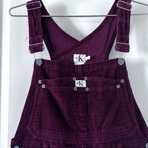 May include: A white ceramic mug with a black handle and the text "But First, Coffee" in a bold, black font. The mug is set against a blurred background, suggesting a cosy setting.