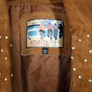 May include: Brown suede jacket with gold studs. The jacket has a label that reads "Atlantic Beach Leather Goat Works" and "Made in China".