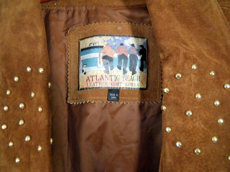 May include: Brown suede jacket with gold studs. The jacket has a label that reads "Atlantic Beach Leather Goat Works" and "Made in China".