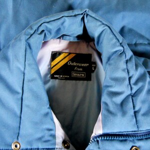 May include: A blue puffer jacket with a zipper closure and a label that reads "Outerwear from Sears" with gold stripes. The label also says "Made in Korea" and "Size L".