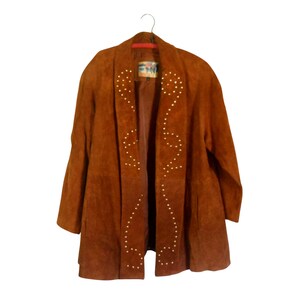 May include: A brown suede jacket with gold studs in a geometric pattern. The jacket has a shawl collar and long sleeves.