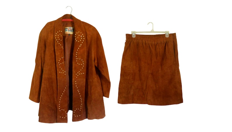May include: A brown suede jacket and skirt set. The jacket has a shawl collar and is decorated with gold studs in a geometric pattern. The skirt is a-line and has a simple design.
