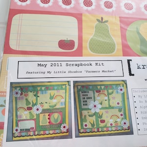 May include: A May 2011 scrapbook kit titled Farmers Market by My Little Shoebox. The packaging features a colorful design with illustrations of pears, tomatoes, and corn, along with two example layouts showing decorative paper, floral accents, and rainbows.