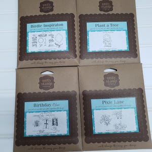 May include: Four stamp sets from Unity Stamp Company. Each set features a brown scalloped frame around a white and blue rectangle with a stamp design and text. The sets are titled "Birdie Inspiration", "Plant a Tree", "Birthday Chic", and "Pixie Lane".