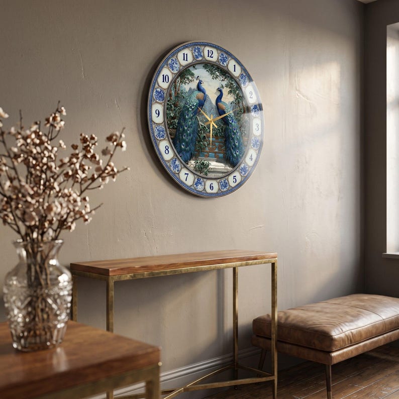 May include: A round wall clock featuring a central illustration of two blue peacocks perched on a stone wall. The clock face has a blue and white floral border with black numerals from 1 to 12 and thin gold-colored clock hands.