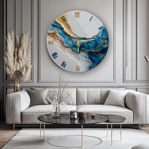May include: A large circular wall clock featuring an abstract design with swirling patterns of deep blue, white, and metallic gold. The clock face displays gold Roman numerals and thin gold hands, set against a smooth, glossy surface finish.
