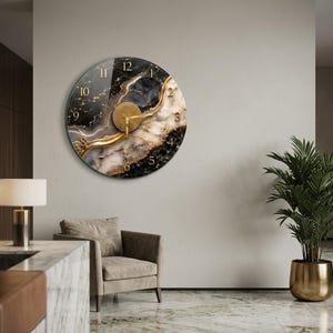 May include: A circular wall clock featuring a swirling black, white, and gold marble-like pattern. The clock face has gold-colored numerals and central hands, with a textured gold circular center piece. The design mimics natural stone veining.