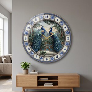 May include: A round wall clock featuring a central illustration of two peacocks perched on a stone ledge amidst trees. The clock face has a blue and white patterned border with black numerals from 1 to 12 and thin gold-colored clock hands.