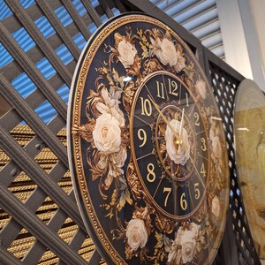 May include: A round wall clock featuring a dark blue background with gold-colored numerals and ornate gold filigree patterns. The clock face is decorated with several cream-colored rose illustrations and has thin gold-colored clock hands.