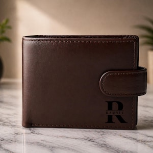 May include: A brown leather wallet with a snap closure. The wallet has the initial "R" and the name "Ramsey" printed on the front. The wallet is rectangular and appears to be new.