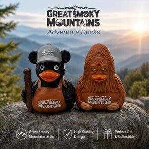 May include: Two novelty rubber ducks with the text "Great Smoky Mountains" on their chests. One is a black duck wearing a hat and overalls, holding a stick. The other is a brown, Sasquatch-like duck.