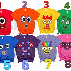 May include: A collection of eight colorful t-shirts, each featuring a different cartoon character face. The shirts are in various colors, including red, orange, yellow, green, blue, purple, and pink. Each shirt has a unique design.