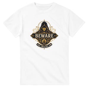 May include: A white short-sleeved t-shirt featuring a central graphic of a hooded figure with a smiling mask. The design includes the text BEWARE and THE SMILING DM in black and gold, along with an illustration of a twenty-sided gaming die.