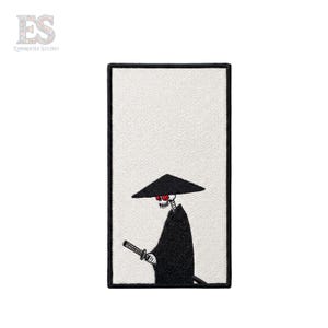 May include: Embroidered patch featuring a skeletal figure in a black robe and conical hat, holding a katana. The figure has red eyes and is set against a white background within a black rectangular border. The patch includes the text "ES EMBROIDER STUDIO".