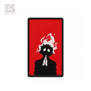 Puede incluir: Un parche rectangular bordado con un fondo rojo vibrante. En el centro, una silueta negra de una figura con cabello blanco en forma de llamas y grandes ojos circulares blancos. La figura muestra las manos juntas en un gesto de oración.