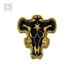 May include: Embroidered patch featuring a black bull skull design with a gold outline and star detail. The patch has a gold border and is likely for clothing or accessories.