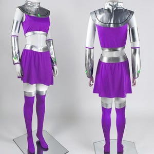 May include: A two-piece purple costume featuring a sleeveless crop top and a skirt with silver metallic trim. The set includes silver arm gauntlets with small green circular accents, a silver collar piece, and matching purple over-the-knee stockings.