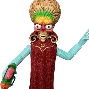 May include: A Martian figure with an oversized, wrinkled, tan-coloured brain, a skeletal face with wide white eyes, and a toothy grin. The figure wears a long, sparkling red cape with gold trim and has light blue arms, holding a green ray gun.