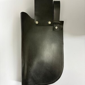 May include: A black leather sheath with a belt loop and a strap. The sheath is designed to hold a knife or similar tool. The edges are stitched with a contrasting thread. The sheath is made of a durable material.