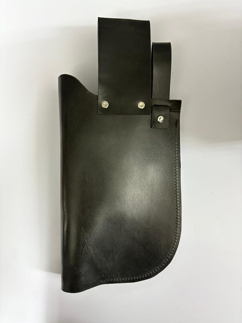 May include: A black leather sheath with a belt loop and a strap. The sheath is designed to hold a knife or similar tool. The edges are stitched with a contrasting thread. The sheath is made of a durable material.