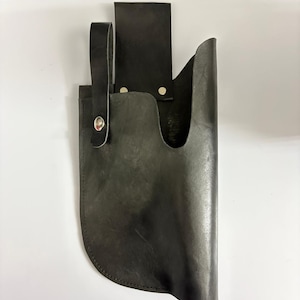 May include: A black leather knife sheath with a loop and a belt loop. The sheath is designed to hold a knife and has a curved bottom. The leather is dark and appears to be well-worn.
