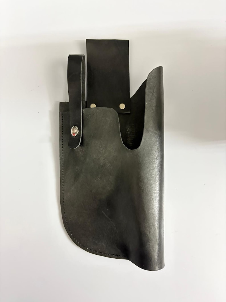 May include: A black leather knife sheath with a loop and a belt loop. The sheath is designed to hold a knife and has a curved bottom. The leather is dark and appears to be well-worn.